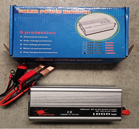 Invertor argintiu Solar Power, etichetat 1000W și 12V DC la 220V AC, lângă cutia albastră și cabluri cu clești.